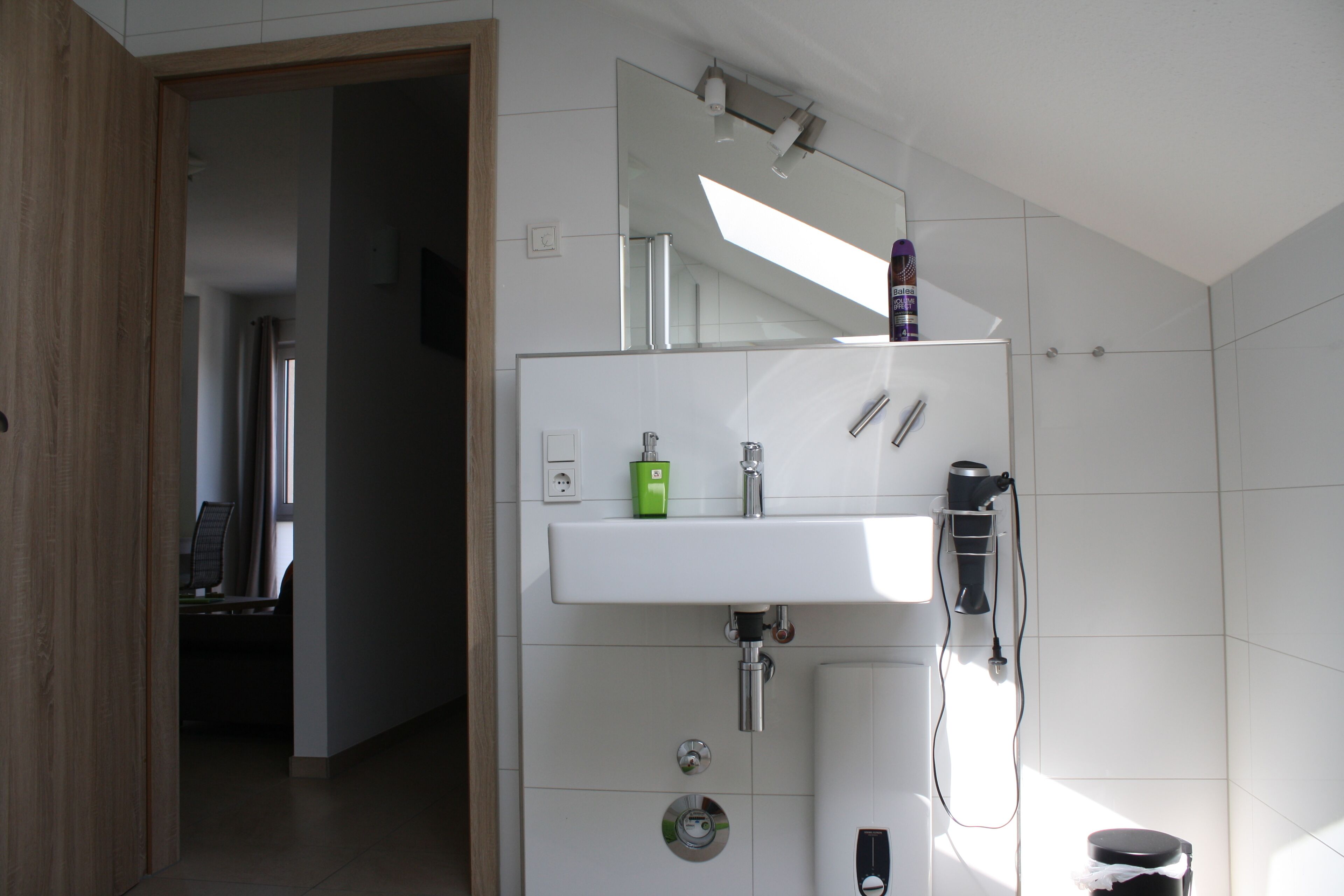 A modern bathroom with a white sink, a mirror, and a hairdryer mounted on the wall.