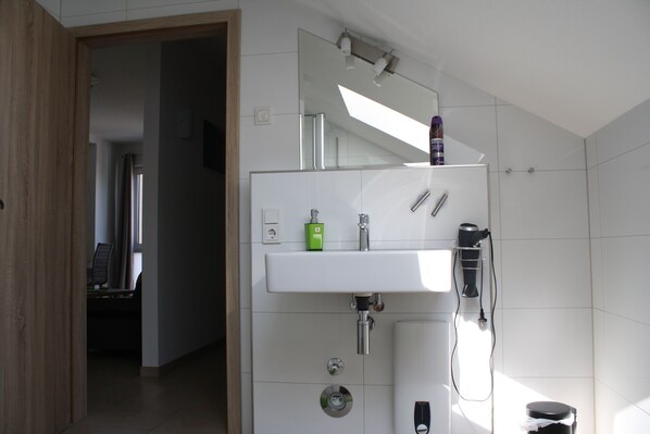 A modern bathroom with a white sink, a mirror, and a hairdryer mounted on the wall. - Cloud 7 I (Heinsberg)