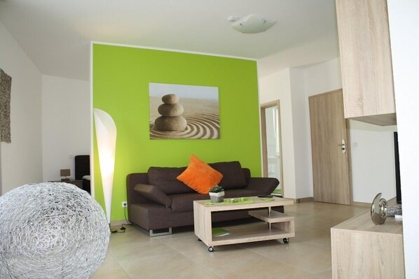 Una sala de estar moderna con una pared verde decorativa, un sofá marrón, una mesa de centro y un objeto decorativo esférico.