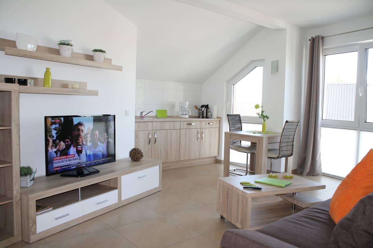 A modern living room with a television, wooden furniture, a dining area, and a large window.