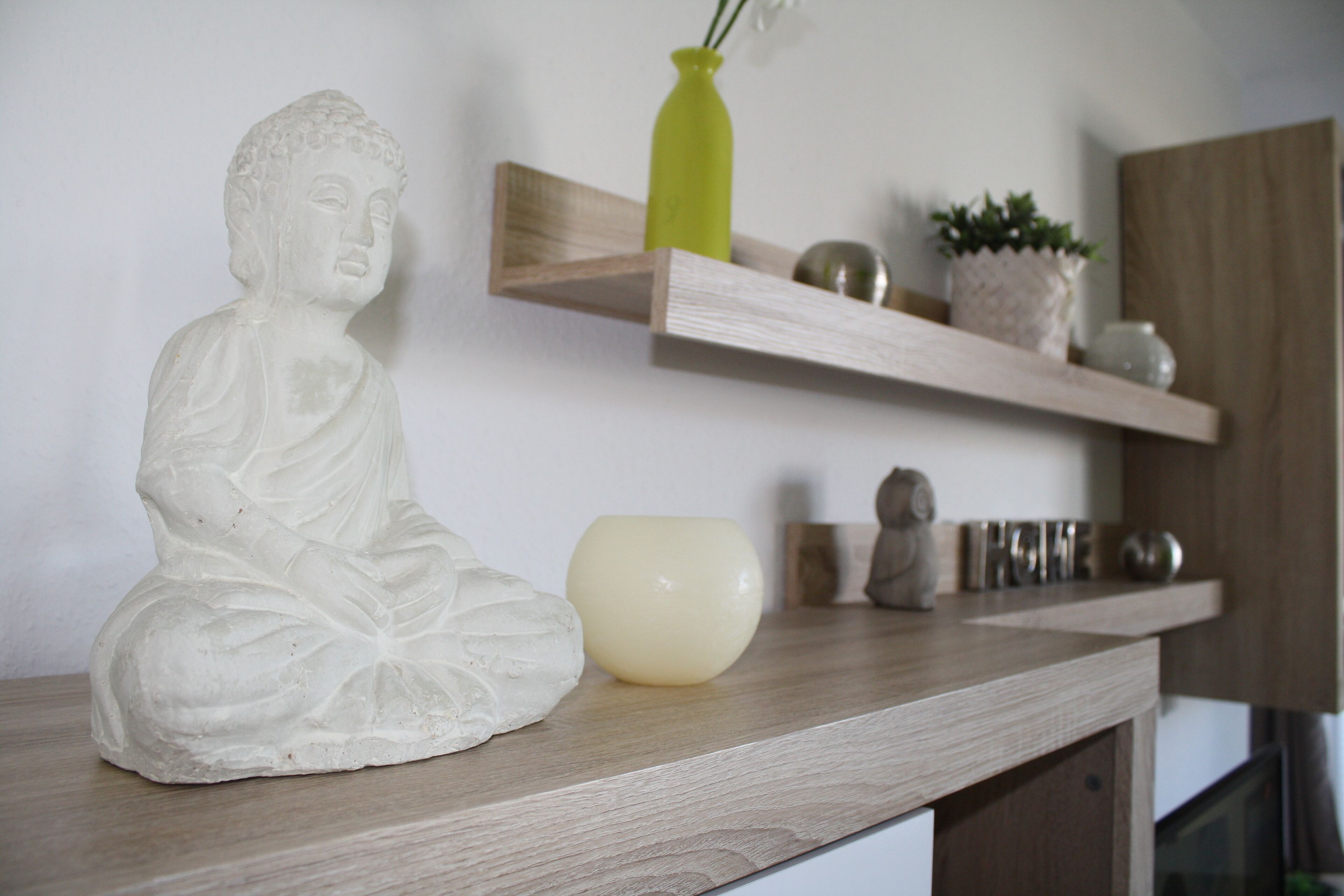 Una statua di una figura seduta su uno scaffale di legno, un vaso verde e una piccola pianta in vaso.