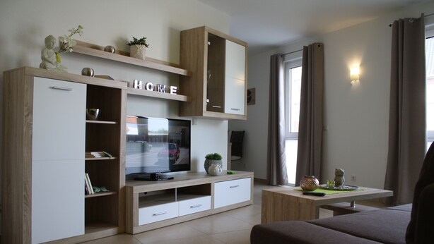 Una sala de estar moderna con un televisor de pantalla plana, armarios de madera, un sofá y una mesita con objetos decorativos.