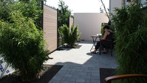 Un patio con mesa y sillas, rodeado de vegetación y un muro bajo.