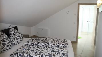 A bedroom with a bed, patterned pillows, a visible door, and a light switch on the wall.