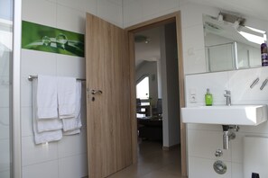 A modern bathroom with a wooden door, white tiles, a sink, and a mirror. - Cloud 7 I (Heinsberg)