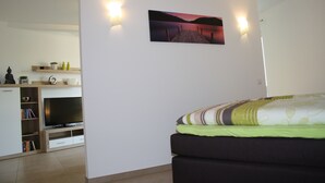 Un dormitorio moderno con cama, televisor de pantalla plana, estante con objetos decorativos y un cuadro colgado en la pared.