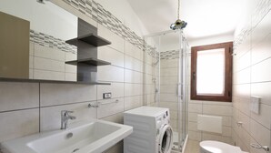 Uma casa de banho moderna com lavatório, máquina de lavar roupa, sanita e cabine de duche.