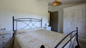 Quarto com cama, mesa de cabeceira, abajur, guarda-roupa e luminária pendente.