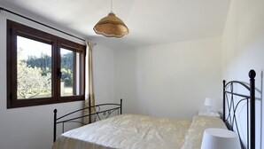Um quarto com cama, mesa de cabeceira com luminária, janela com cortinas e luminária pendente.