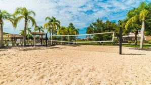 A sandy beach volleyball court with palm trees, a fence, and a building in the background. - Aco8068ha - Bella Vida Resort - 4 Bed 3 Baths Townhome (Kissimmee)