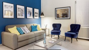 A modern living room with a grey sofa, blue armchairs, and a coffee table. There are framed pictures on the wall and a radiator in the background. - Bluechiaia apartment- close to everything. (Napoli)