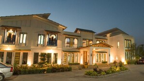 A large, multi-story building with a central entrance, multiple balconies, and a well-lit facade. - Arch The Baakhli Resort (Ramnagar)