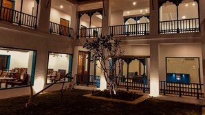 A multi-story building with balconies, a dining area, and a small garden. - Arch The Baakhli Resort (Ramnagar)