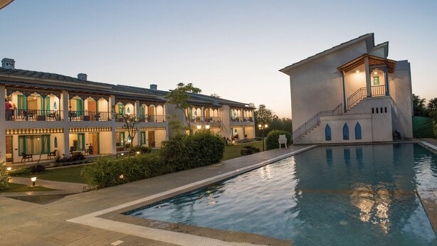 A large, multi-story building with a swimming pool in the foreground. - Arch The Baakhli Resort (Ramnagar)