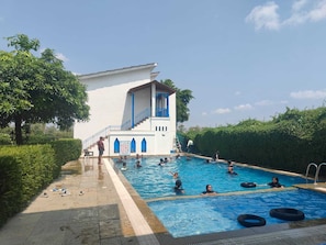 A swimming pool area with a building featuring blue accents and a staircase leading to a balcony.