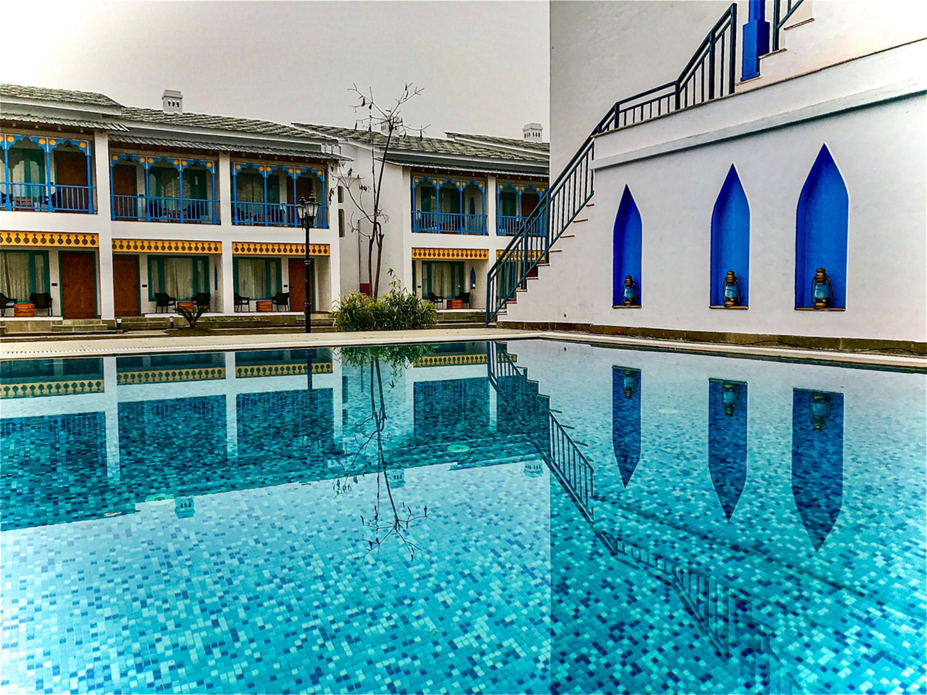 Une piscine à l’eau d’un bleu cristallin, un escalier menant à un balcon, et un bâtiment doté de nombreux balcons et fenêtres.