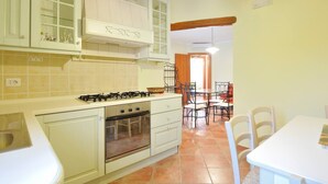 A kitchen with white cabinets, a gas stove, an oven, and a dining area with a table and chairs. - Armandiola 3 apartment (Cardedu)