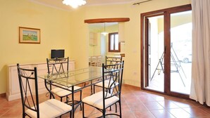 A dining area with a glass table and chairs, a television on a stand, and a painting on the wall. - Armandiola 3 apartment (Cardedu)