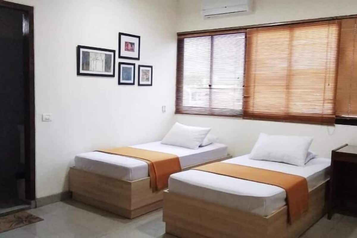 Una habitación con dos camas individuales, un escritorio pequeño, una ventana con persianas y una puerta.