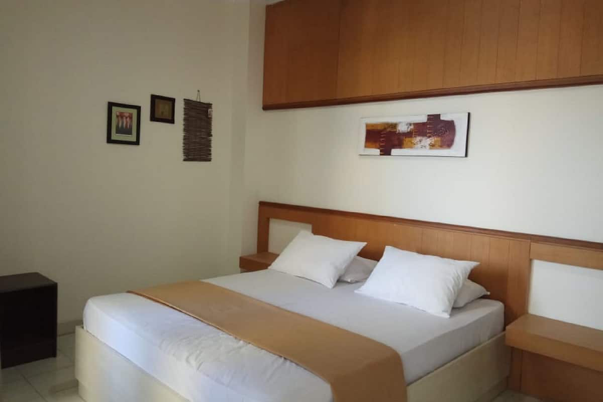 Un dormitorio ordenado con una cama grande, un cabecero de madera y una mesita de noche pequeña.