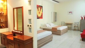Ein Hotelzimmer mit einem Holzkoffer, zwei Betten, einem kleinen Schreibtisch und einem Kühlschrank.