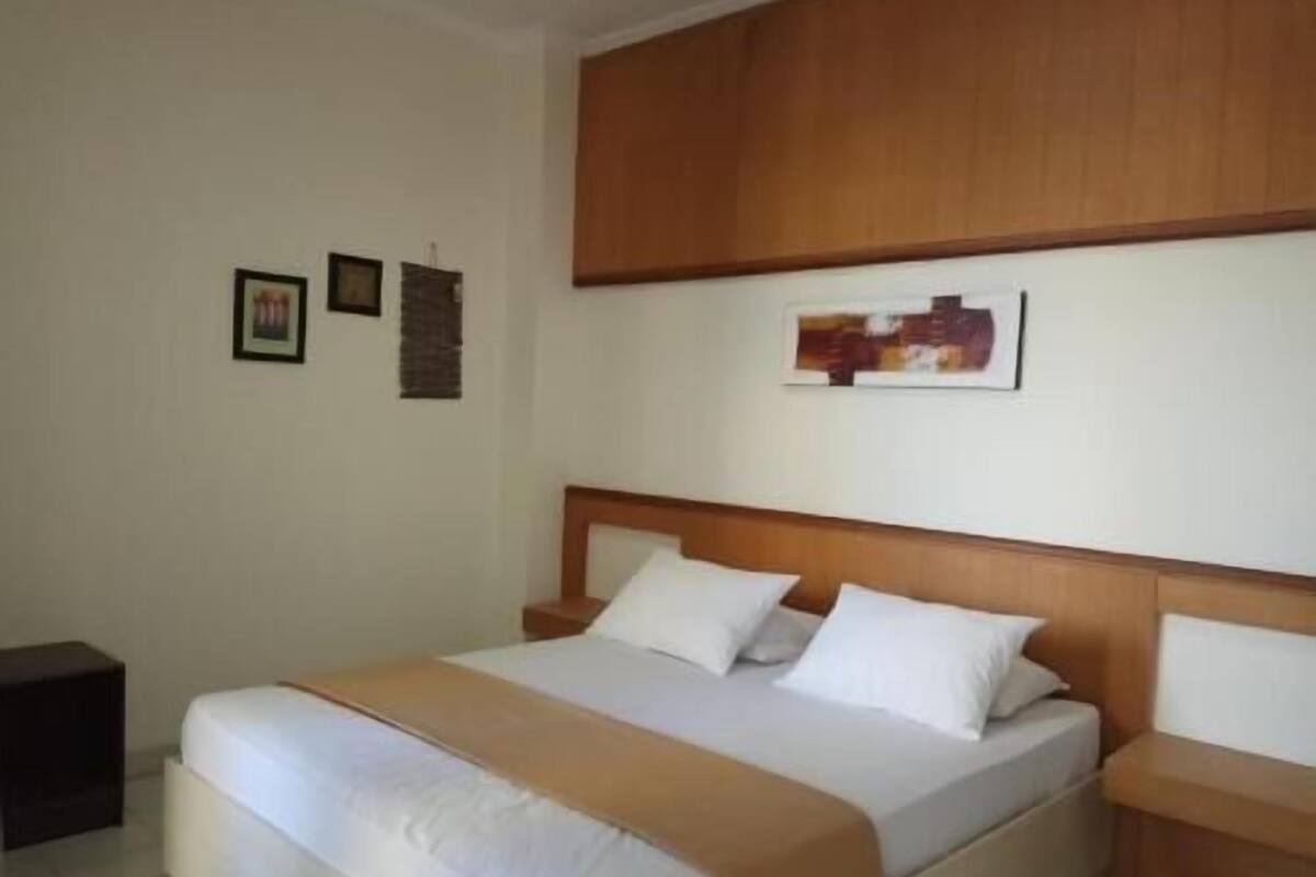 Una habitación de hotel con una cama, un cabecero de madera, una mesita de noche y una obra de arte colgada en la pared.