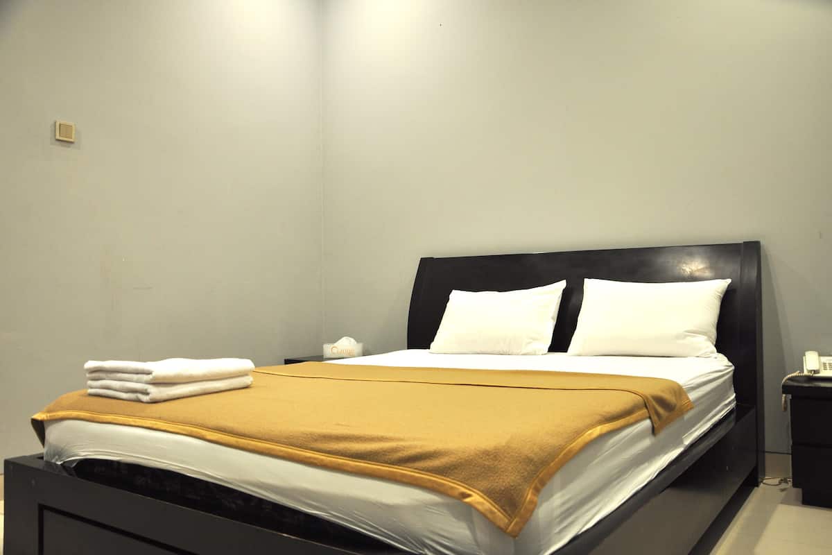 A neatly made bed with white linens and a mustard-colored blanket, a bedside table with a phone, and a wall-mounted light fixture.