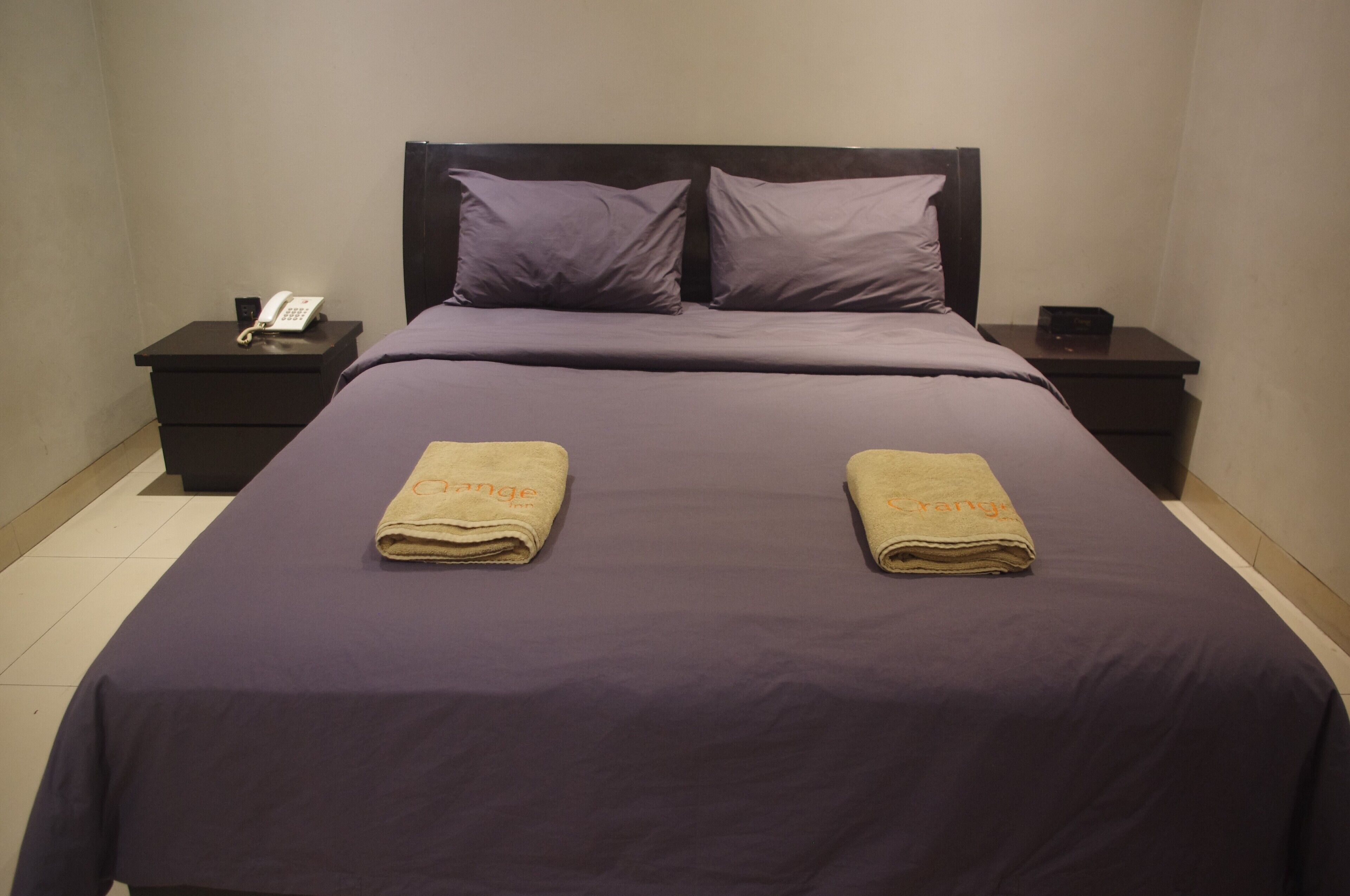 A hotel room with a bed, two nightstands, a telephone, and two towels with the word "range" on them.