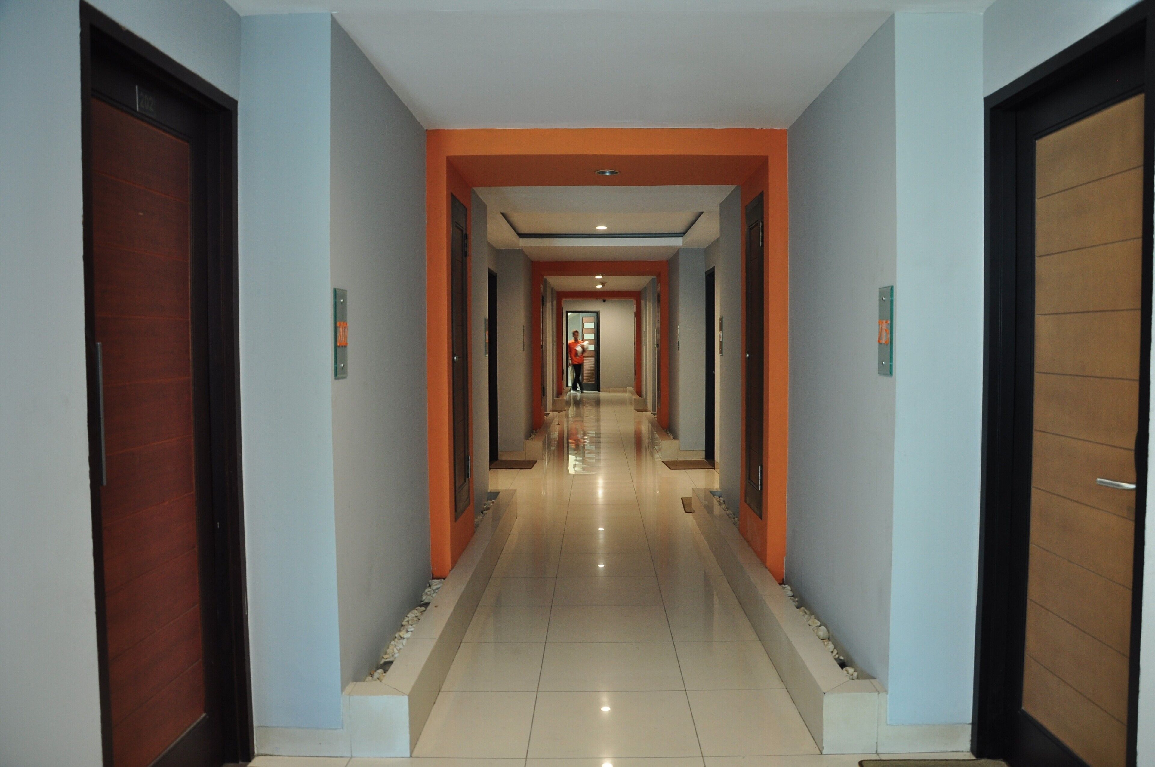 A hotel corridor with multiple doors, a tiled floor, and orange accents on the walls.