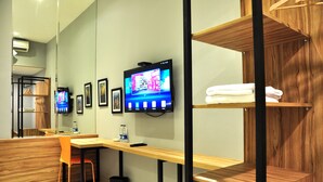 Un baño moderno con tocador de madera, un espejo, televisor montado en la pared y repisas con toallas dobladas.