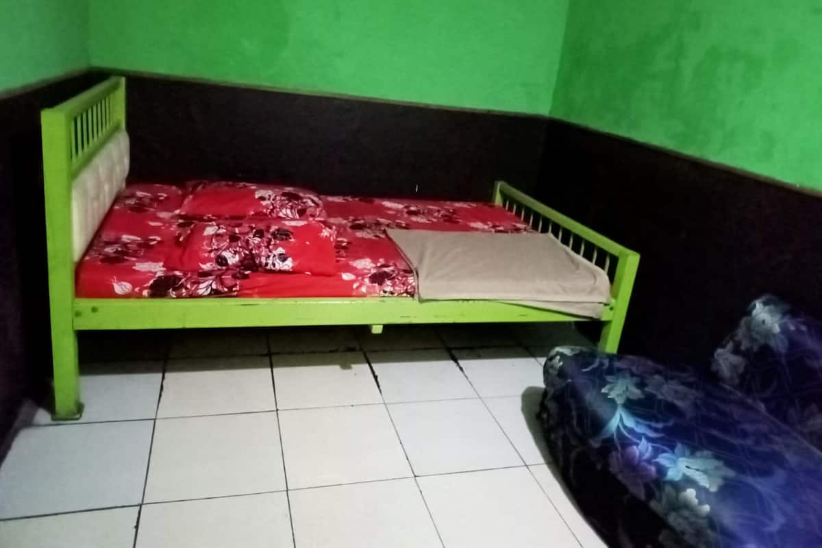 A small, single-bed room with green walls and a tiled floor.