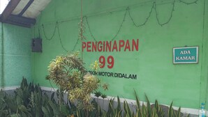 Un edificio verde con un letrero que dice "PENGINAPAN 99 PARKIR MOTOR DIDALAM" y otro letrero que dice "ADA KAMAR".