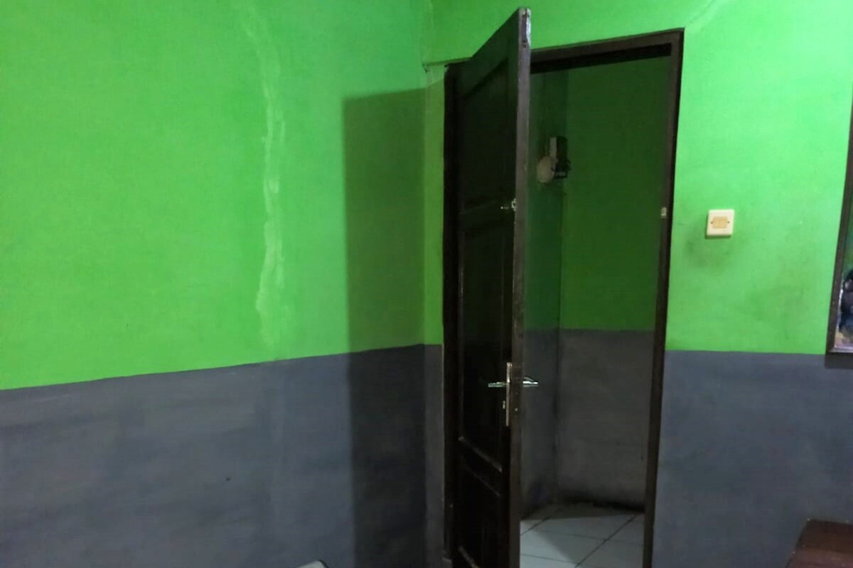 A room with green and grey walls, a tiled floor, a black door, and a small trash bin.