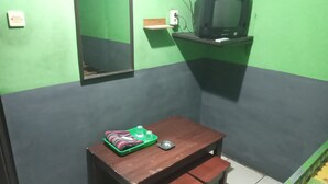Una habitación pequeña con una mesa y banco de madera, pared verde, televisor montado y un espejo.