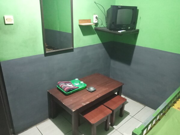 A small room with a wooden table, a bench, a television on a stand, and a green wall. - Penginapan 99 (Bandung)