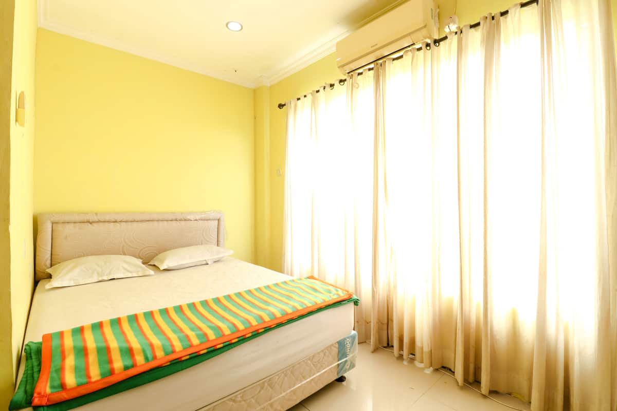 A bed with a striped blanket, a headboard, and a window with curtains.