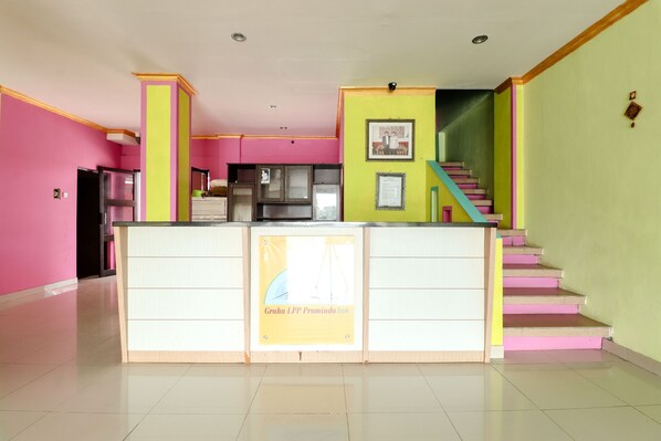 A hotel lobby with a reception desk, a staircase, and a green wall.
