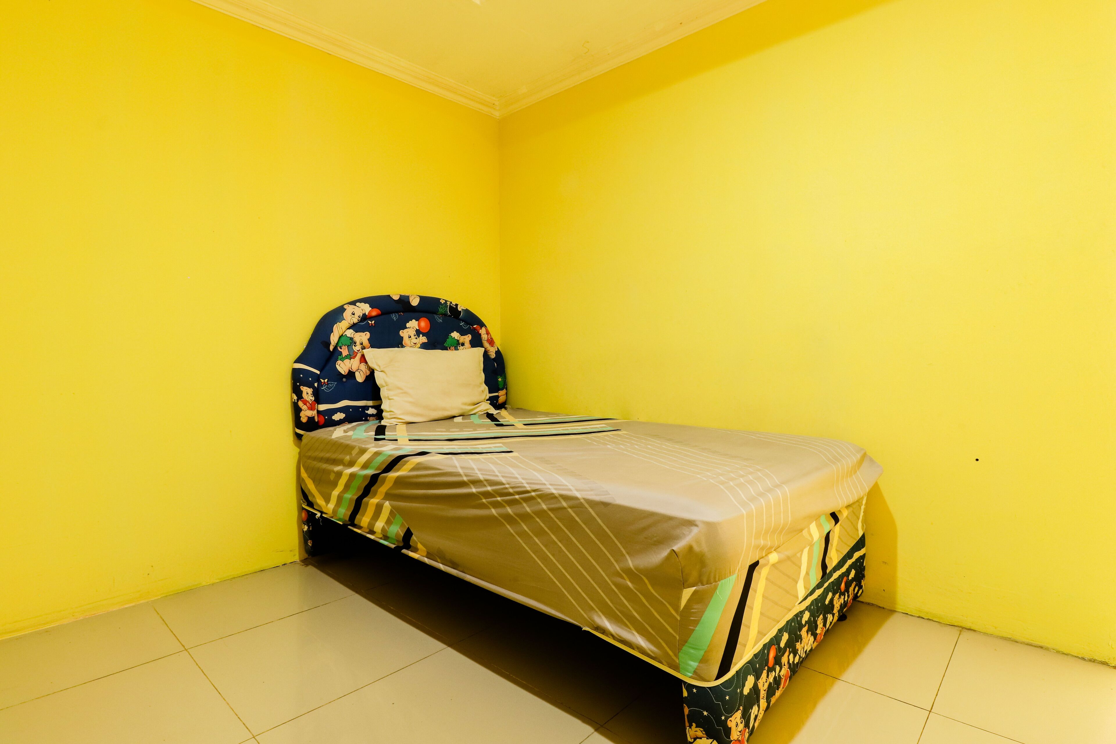 Una habitación pequeña con una cama individual, pared amarilla y techo blanco liso.