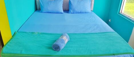 A bed with a blue mattress and pillows, a green blanket, and a rolled towel.