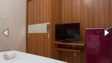 A hotel room with a bed, a television, a wooden wardrobe, and a refrigerator.