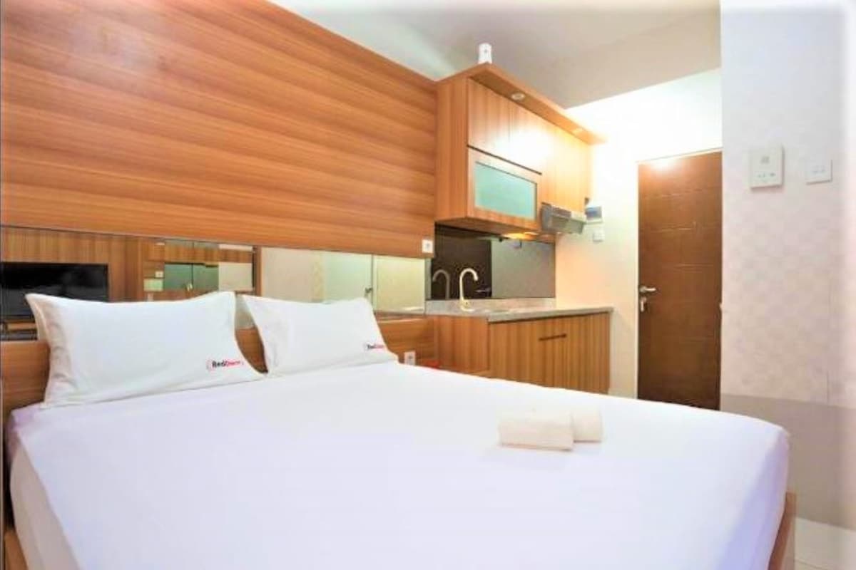 A hotel room with a bed, a wooden headboard, a small kitchenette, and a door.