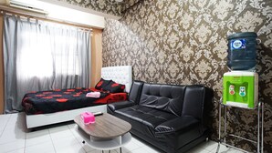 A room with a bed, a black leather sofa, a small table, and a water dispenser. - City Park Apartment by Anita (Jakarta)