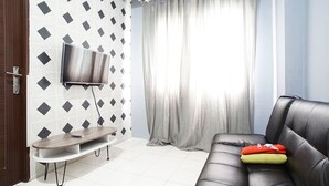 A living room with a flat-screen TV mounted on a wall, a sofa with cushions, and a small table with a remote control. - City Park Apartment by Anita (Jakarta)
