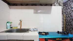 A kitchen with white tiles, a stainless steel sink, a blue gas stove, and a measuring tape on the wall. - City Park Apartment by Anita (Jakarta)
