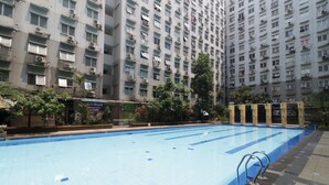 A swimming pool with a tiled deck, surrounded by a high-rise residential building with multiple balconies and air conditioning units. - City Park Apartment by Anita (Jakarta)