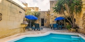 A pool area with stone walls, two blue umbrellas, and outdoor seating.
