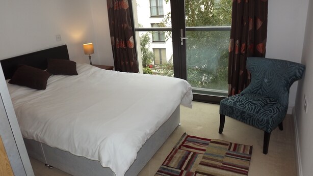 A hotel room with a large bed, a chair, a lamp, and a view of the outside. - 55 St James Walk (Cheltenham)