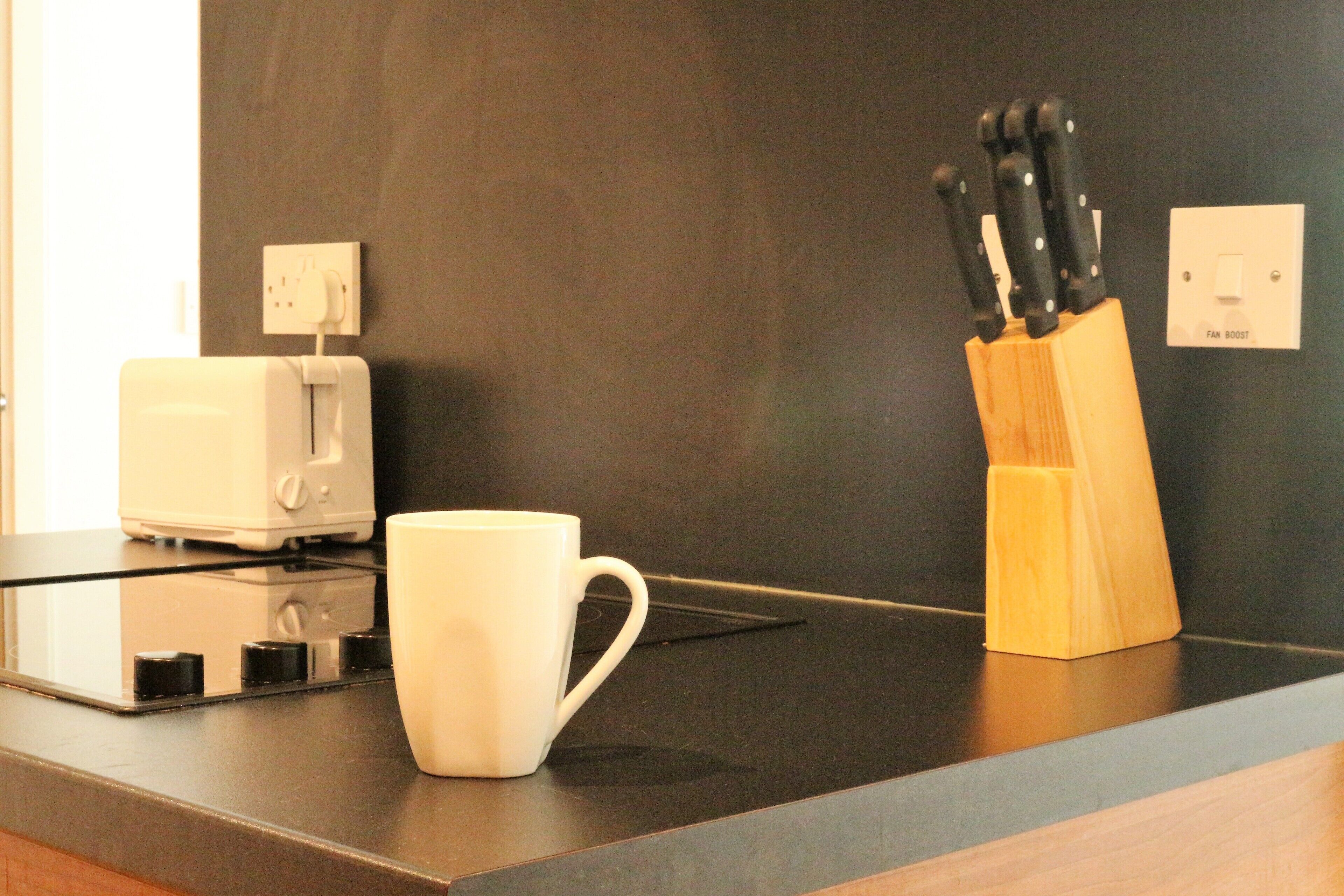 A kitchen counter with a white mug, a toaster, and a knife block.