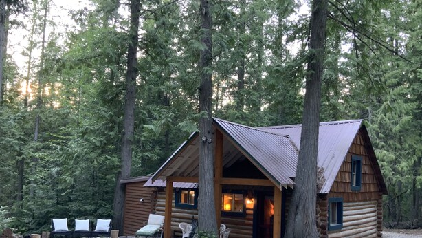 A log cabin with a porch, surrounded by trees. - Stylish Cabin in 12 Acres of Private Forest (Sagle)