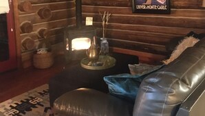 A cozy living room with a fireplace, a leather sofa, and a rustic wooden wall. - Stylish Cabin in 12 Acres of Private Forest (Sagle)